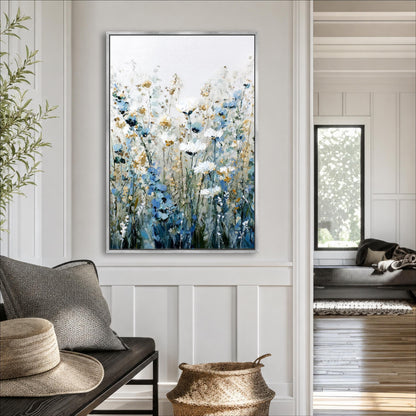 a living room with a large painting of a field of flowers hanging on the wall. The painting has a white background with blue and yellow flowers, creating a serene and natural atmosphere. The room is furnished with a couch, a wicker basket, and a hat, adding to the cozy and inviting ambiance.