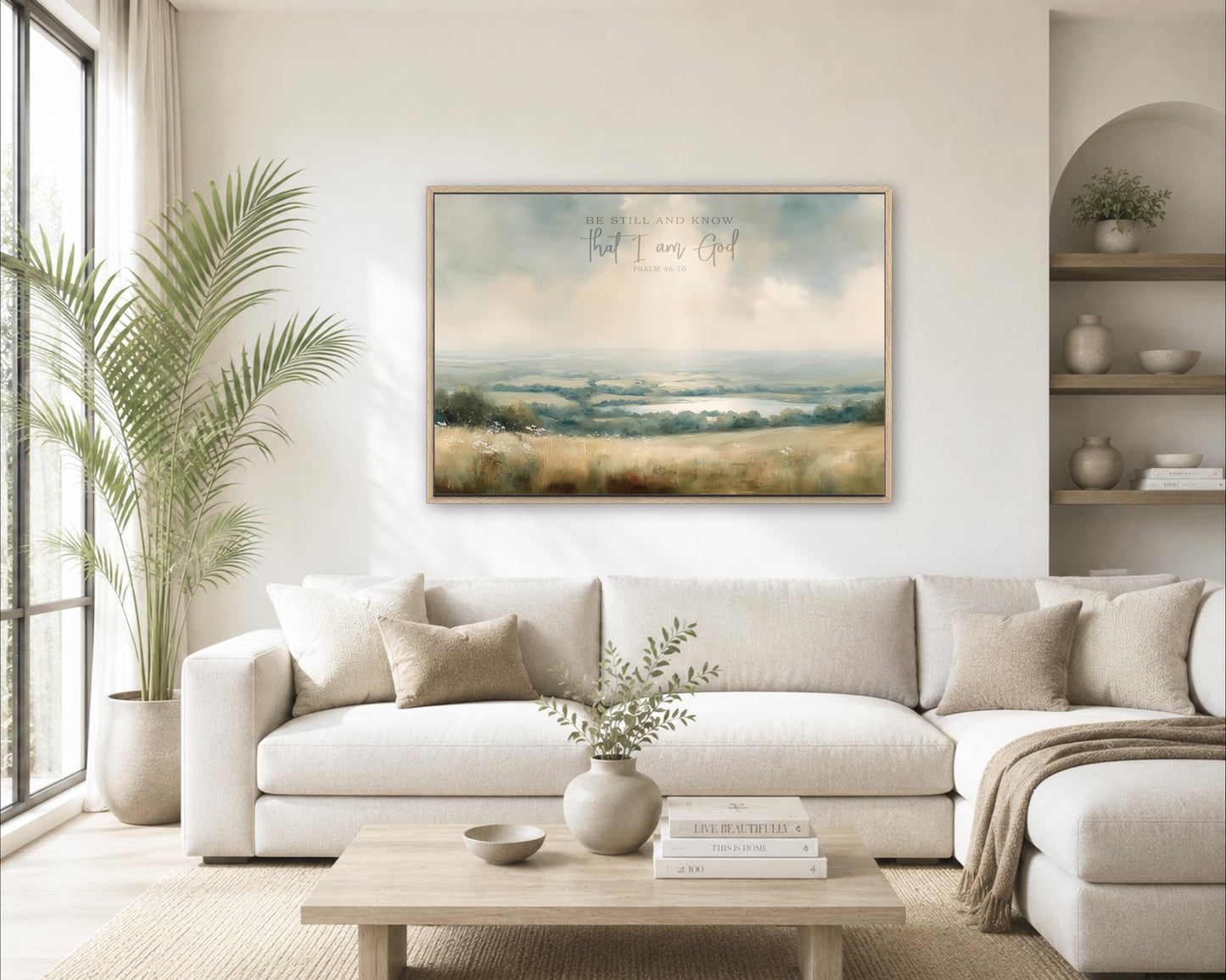 a cozy living room with a large, framed landscape painting hanging on the wall above a white sofa. The painting features a serene countryside scene with rolling hills and a tranquil body of water. The room is decorated with various plants, vases, and books, creating a warm and inviting atmosphere.