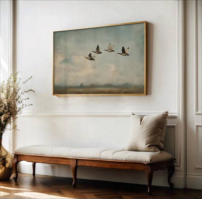 a large painting of three ducks flying in formation on a white wall, with a wooden bench and a vase of flowers placed in front of it.