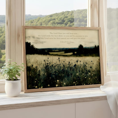 a framed photograph of a serene landscape with a field of flowers and trees, set against a backdrop of a mountainous landscape. The photograph is framed in a wooden frame and is placed on a windowsill.