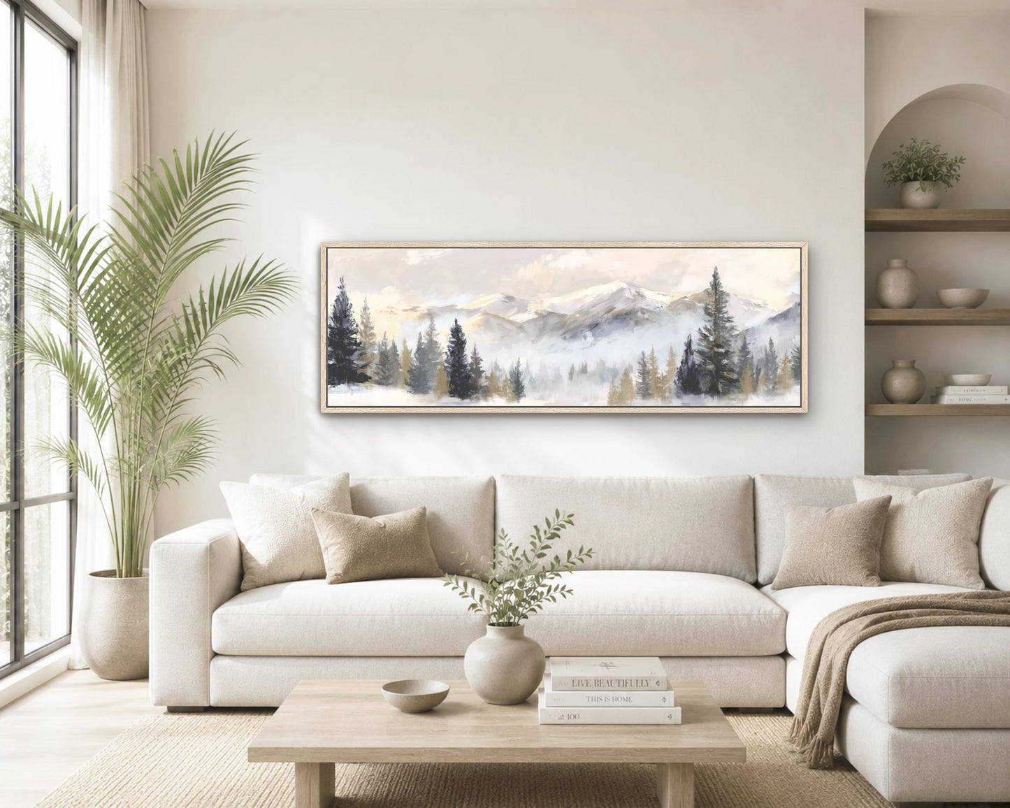 a serene living room with a large painting of a mountain landscape hanging on the wall above a white sofa. The sofa is adorned with throw pillows and a vase of greenery, creating a cozy and inviting atmosphere. The room also features a coffee table with books and a potted plant, adding to the overall aesthetic and comfort of the space.