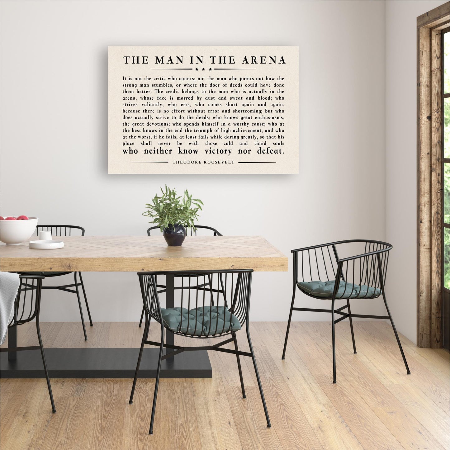 a framed quote by Theodore Roosevelt, "The Man in the Arena", displayed on a wall above a wooden dining table with black chairs.