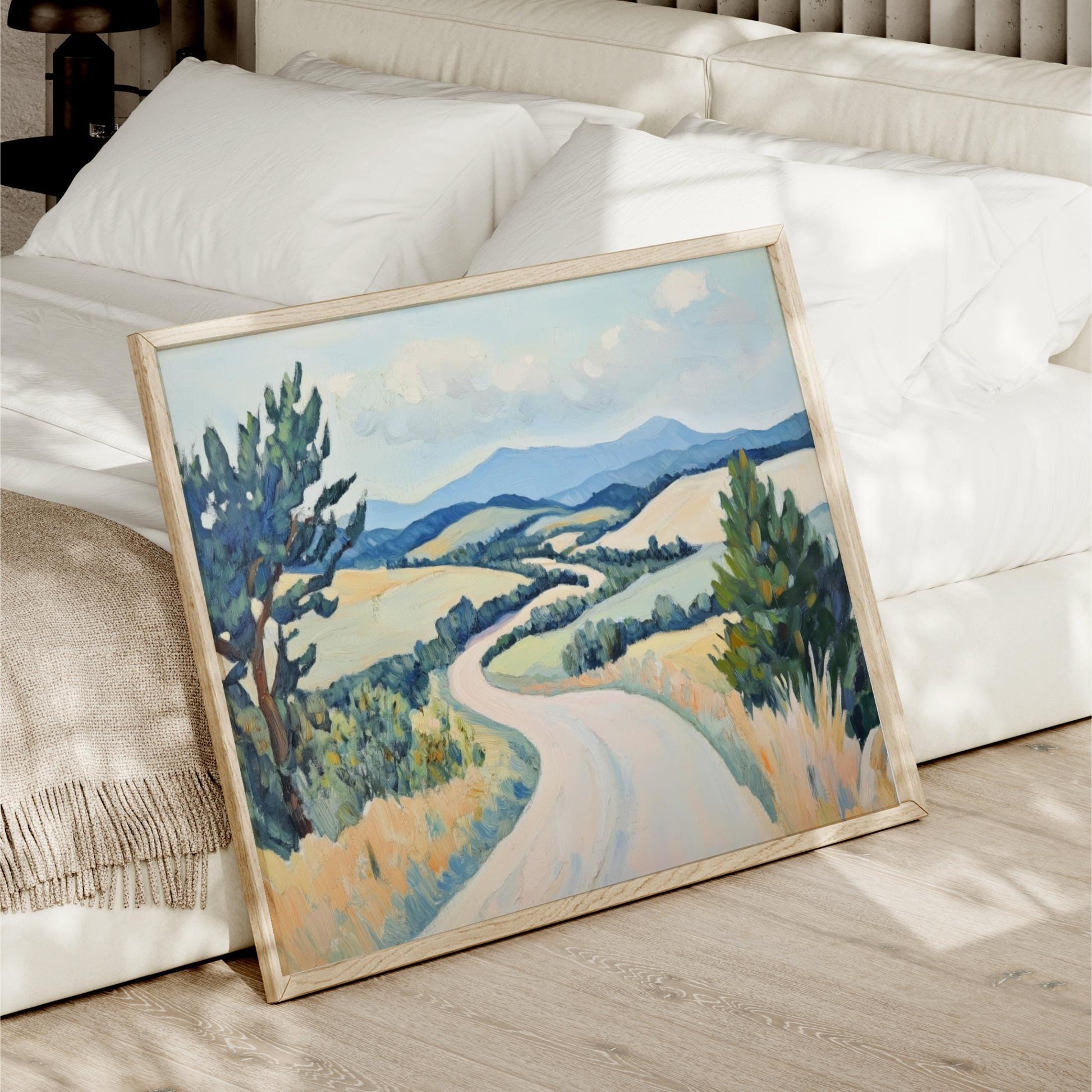 A framed landscape painting depicting a winding road through a countryside scene with trees, hills, and a blue sky with clouds.