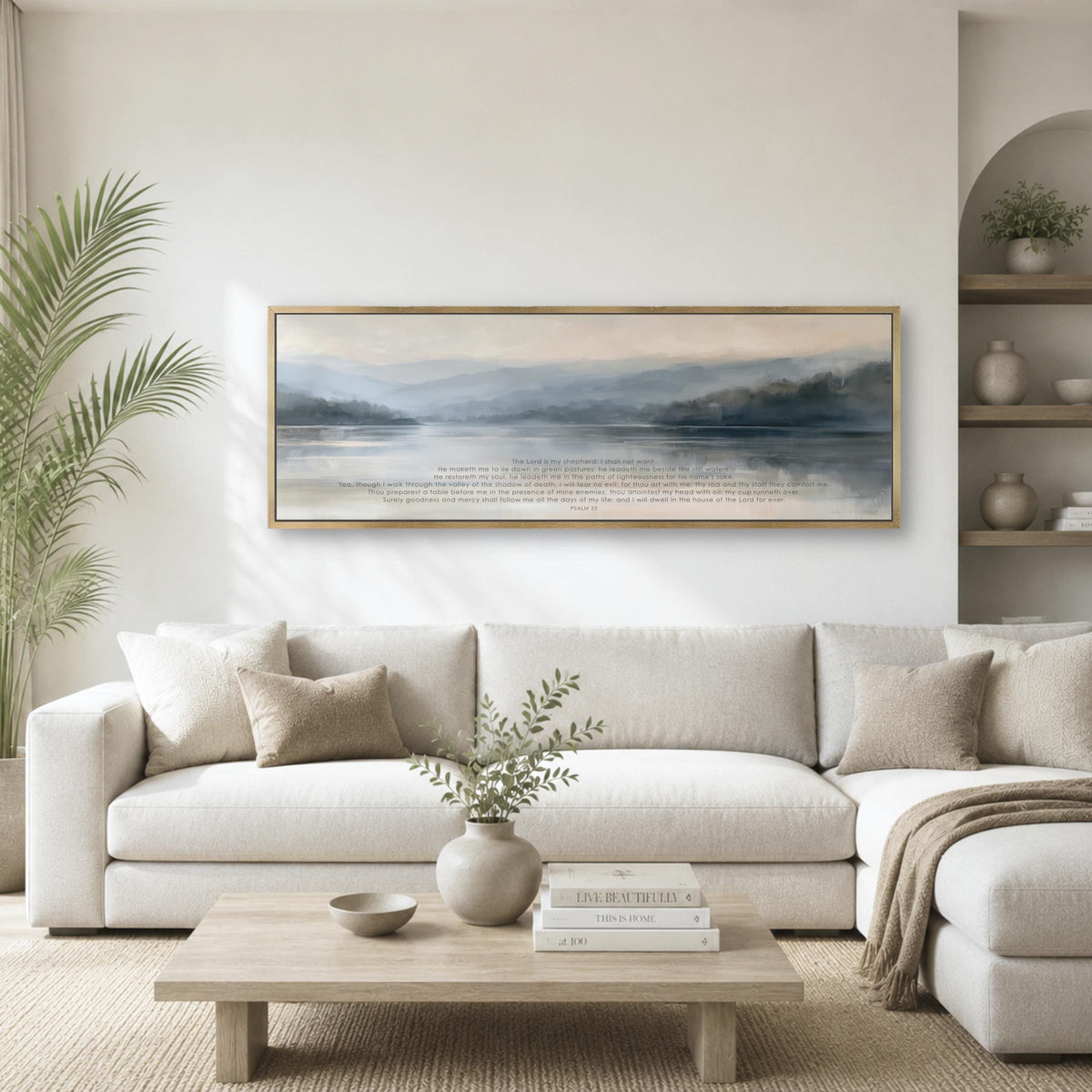 a serene living room with a large, framed painting of a tranquil landscape hanging on the wall above a white sofa. The sofa is adorned with throw pillows and a vase of greenery, creating a cozy and inviting atmosphere. The room also features a coffee table with decorative items, and a bookshelf with books and other decorative objects.