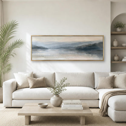 a serene living room with a large, framed painting of a tranquil landscape hanging on the wall above a white sofa. The sofa is adorned with throw pillows and a vase of greenery, creating a cozy and inviting atmosphere. The room also features a coffee table with decorative items, and a bookshelf with books and other decorative objects.