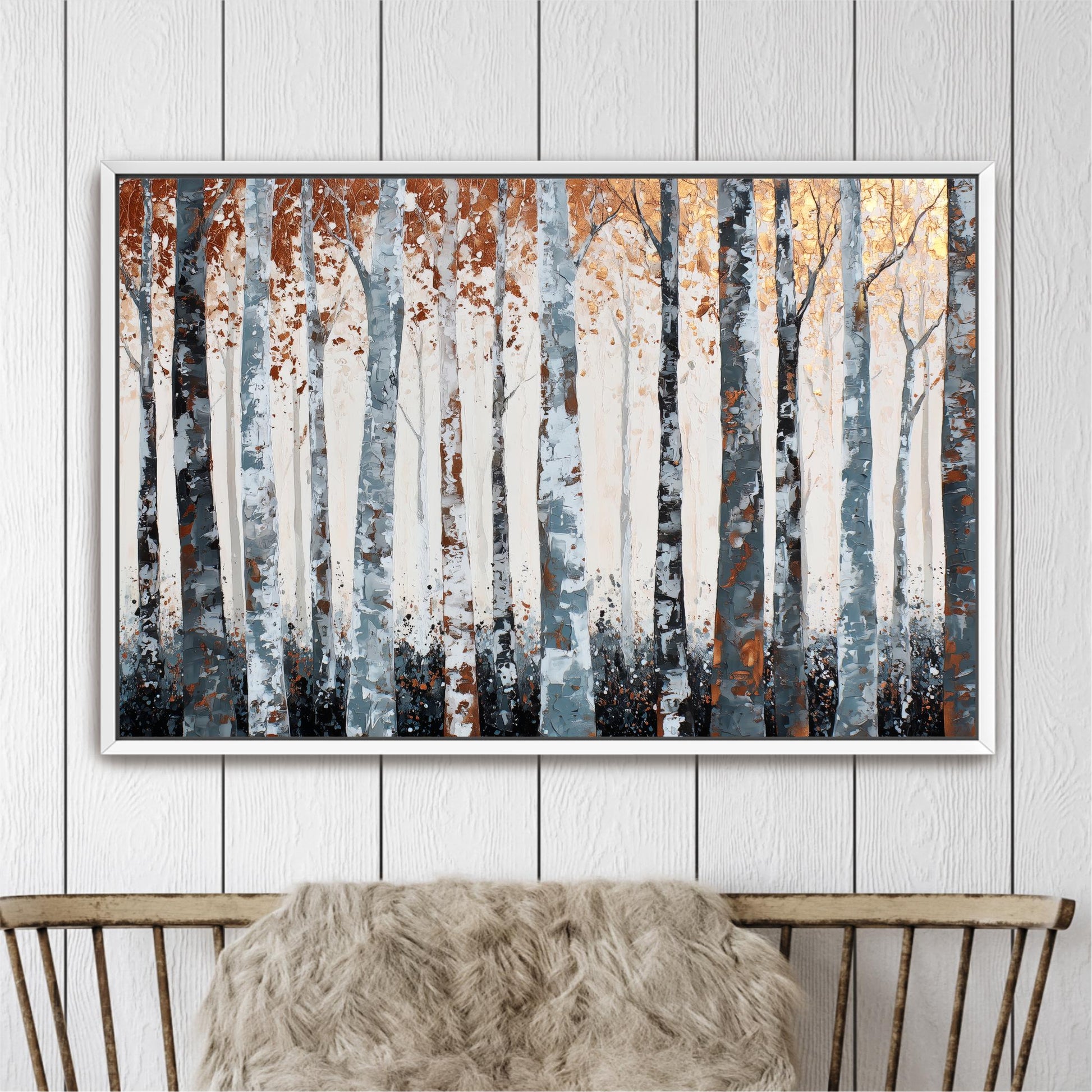 a large painting of a forest with tall trees in shades of white, gray, and orange. The painting is displayed on a white wall above a wooden chair.