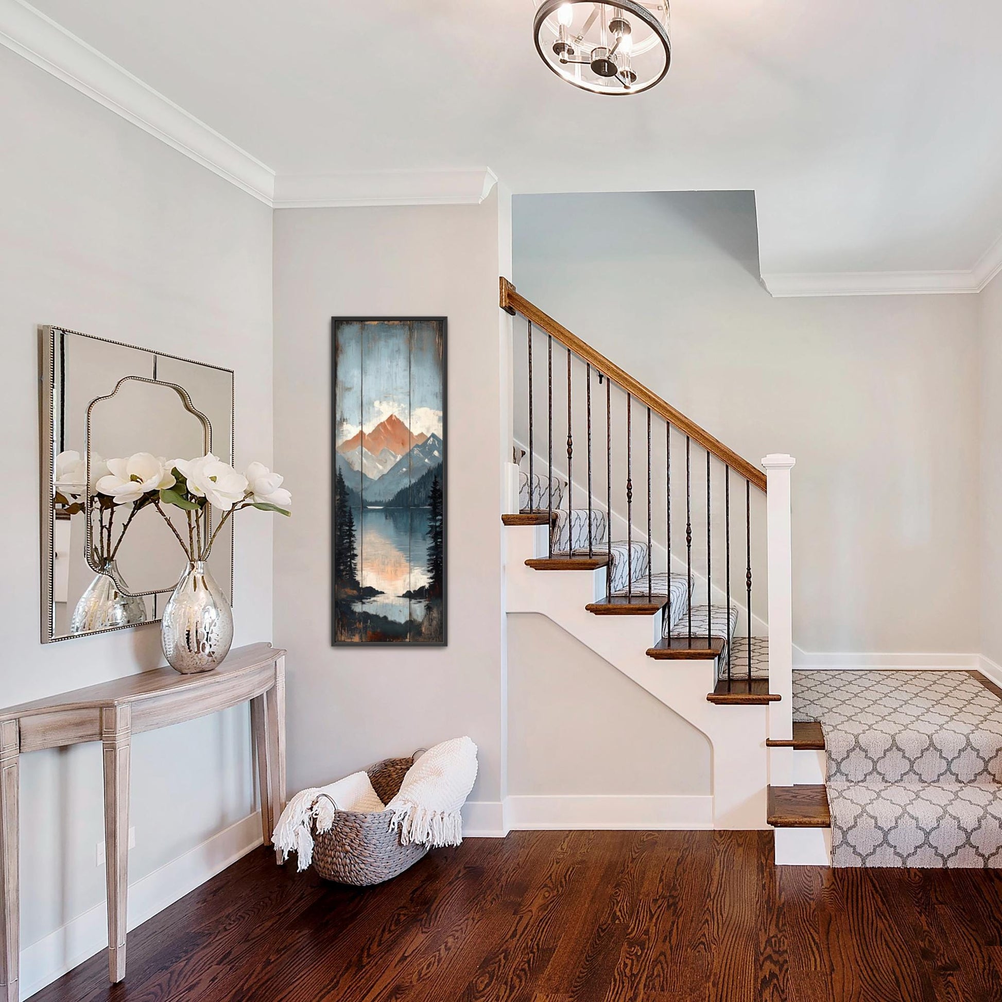 a well-lit and organized entryway with a wooden staircase, a mirror, a console table with a vase of flowers, and a painting of a mountain landscape.
