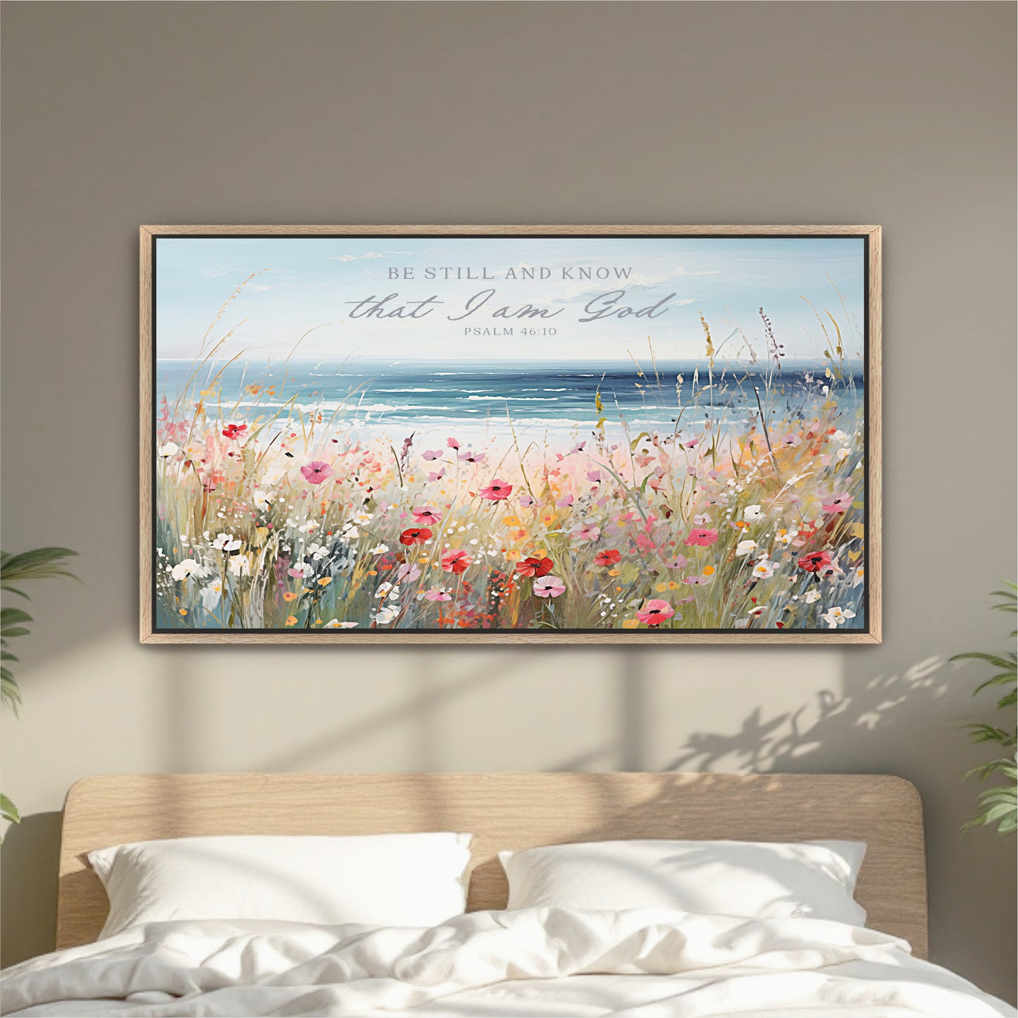 a framed painting of a field of flowers with a body of water in the background, hanging on a wall above a bed.