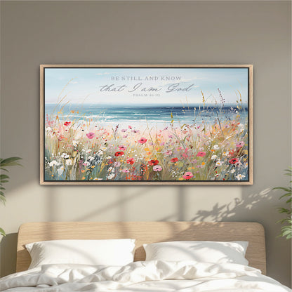 a framed painting of a field of flowers with a body of water in the background, hanging on a wall above a bed.