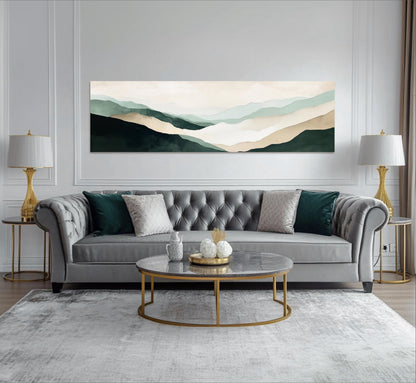 a modern living room with a gray tufted sofa, a round marble coffee table, and two gold side tables with lamps. Above the sofa, there is a large landscape painting depicting a mountain range with a light blue sky.