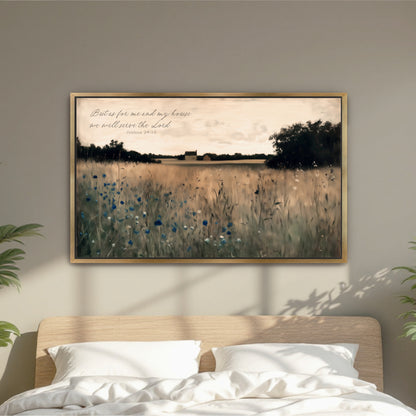 A framed painting of a field with tall grass and blue flowers hangs on a wall above a bed with white pillows.
