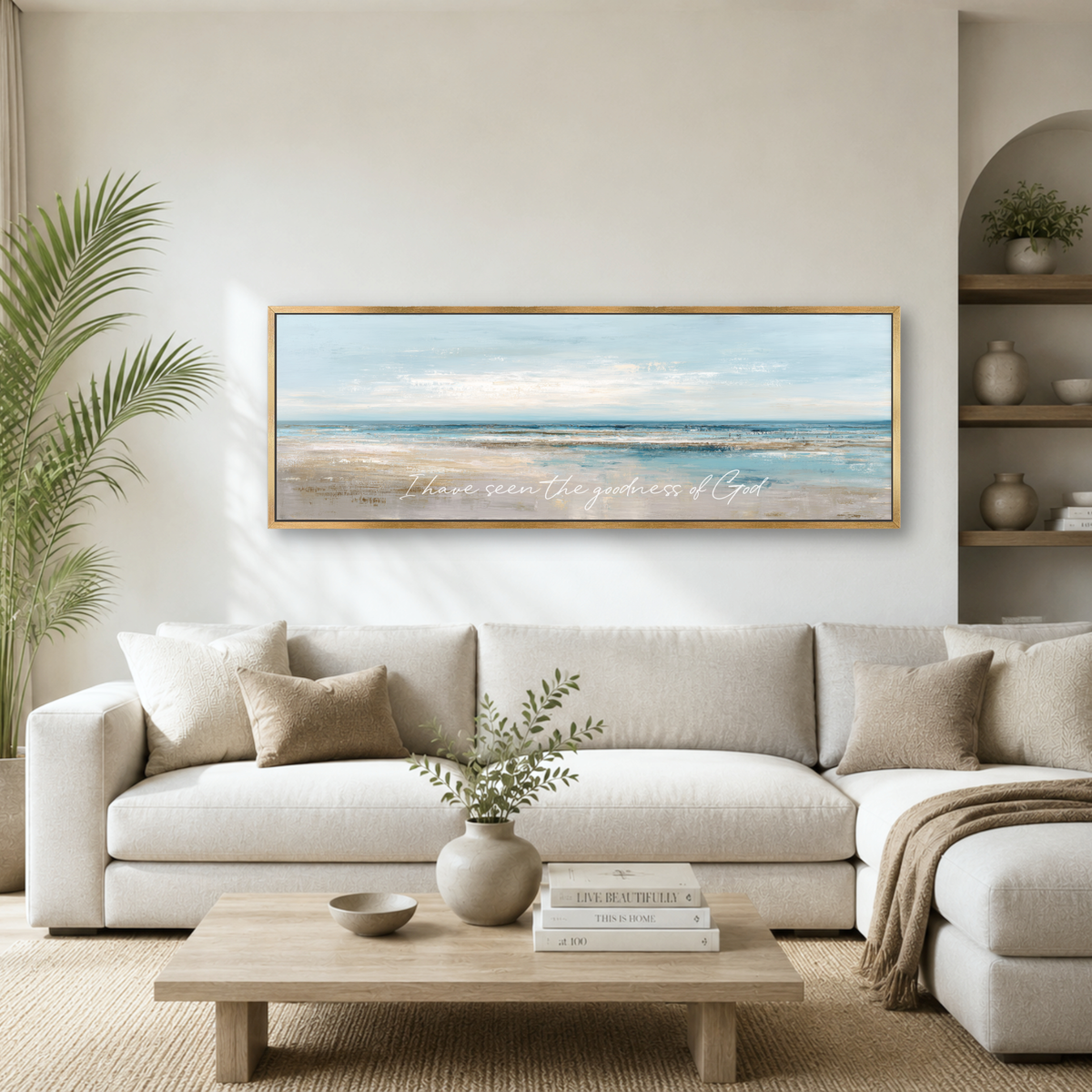 a living room with a large framed painting of a beach scene hanging on the wall above a white sofa. The painting depicts a serene beach landscape with a clear blue sky and calm ocean. The room is decorated with various items, including a potted plant, a vase with greenery, and a stack of books. The overall atmosphere of the room is calm and inviting, with the beach scene as the focal point.
