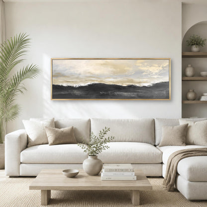 a modern living room with a large, framed landscape painting hanging on the wall above a white sofa. The painting features a serene landscape with a cloudy sky and rolling hills. The room is decorated with a wooden coffee table, a vase with greenery, and a stack of books. The overall color scheme is neutral, with the white sofa and wooden furniture creating a calm and inviting atmosphere.