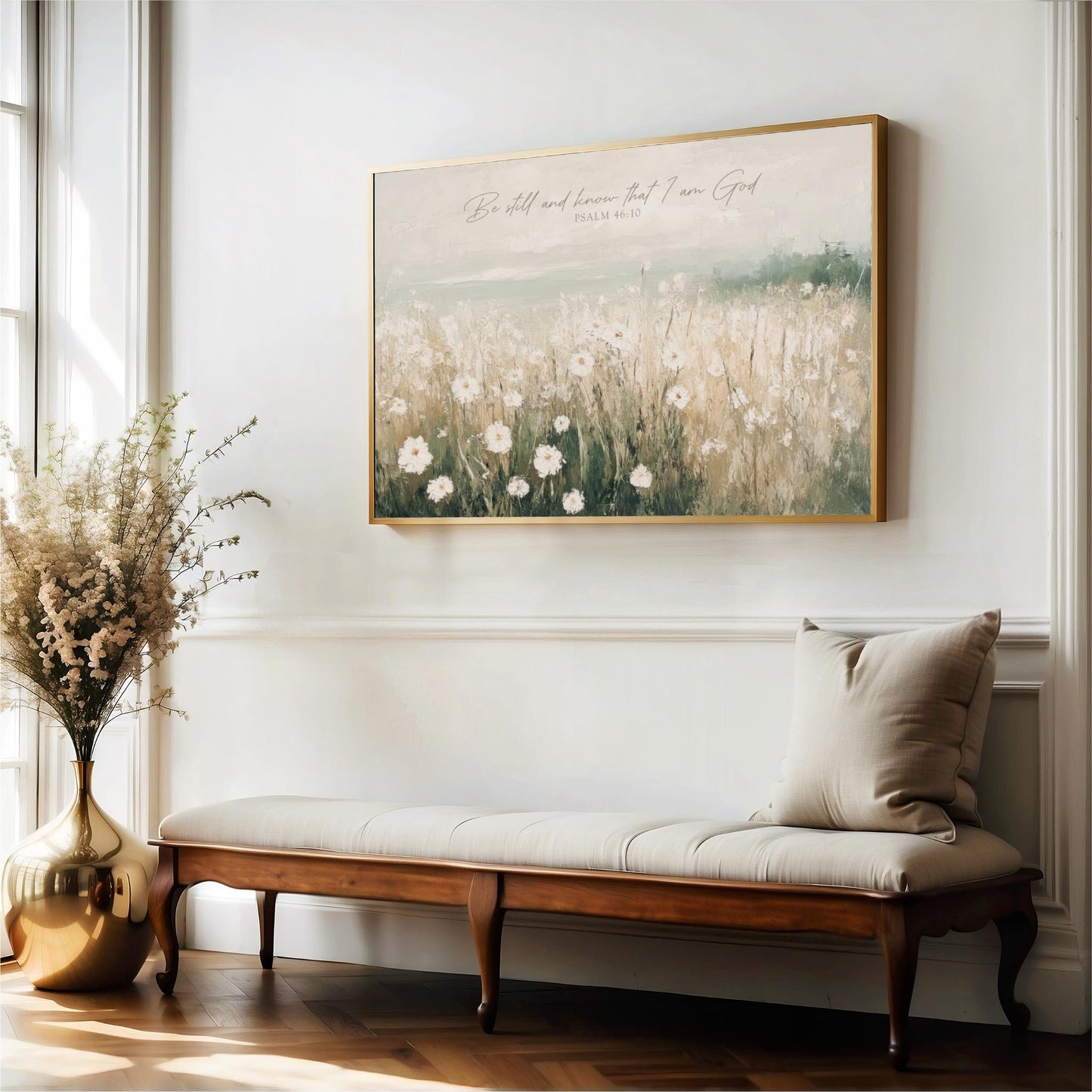 a serene indoor setting with a large painting of a field of flowers hanging on the wall above a wooden bench. The painting is framed in gold and has a Bible verse from Psalm 46:10 displayed on it. The bench is positioned in front of the painting, and there is a vase of flowers on the floor next to it.