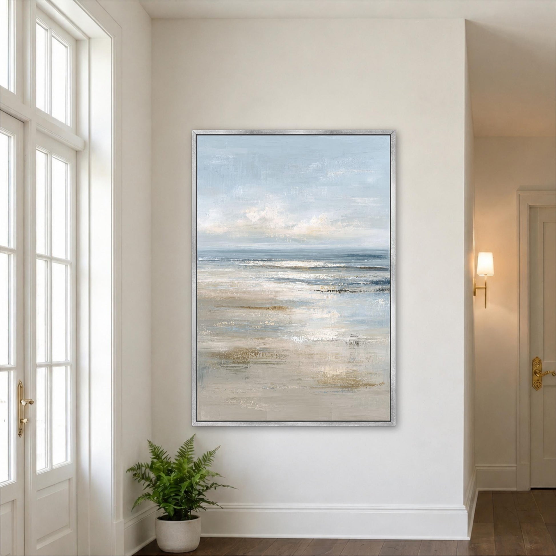 a large painting of a serene beach scene hanging on a white wall in a room with a large window.
