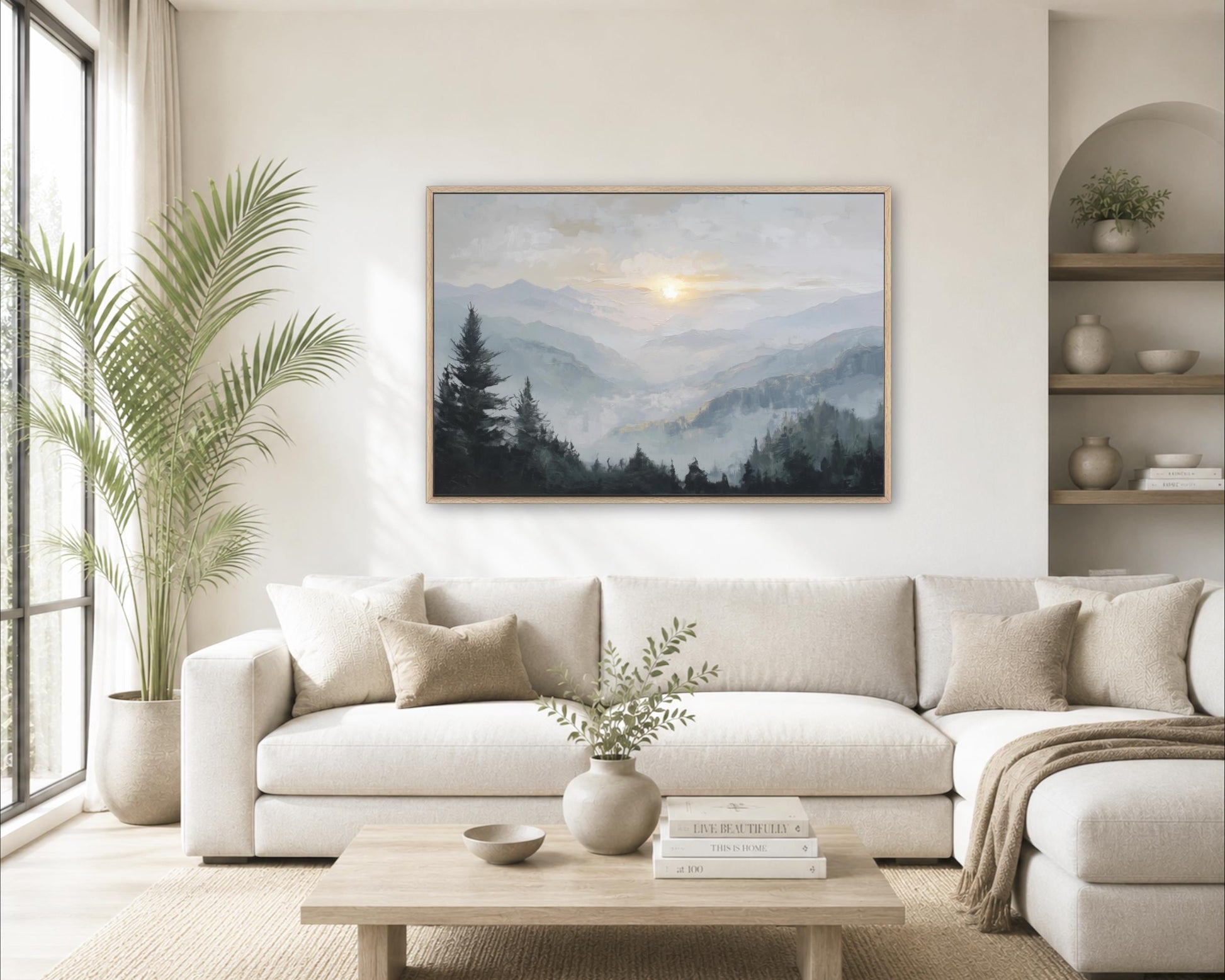 a serene living room with a large painting of a mountain landscape hanging on the wall above a white sofa. The room is decorated with a potted plant, a vase with greenery, and a stack of books on the coffee table.