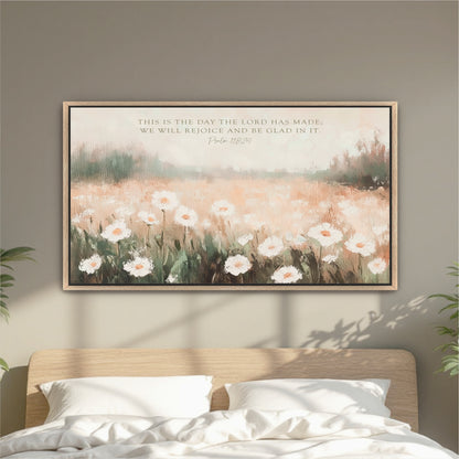 a framed painting of a field of white flowers hanging on a wall above a bed with white pillows.