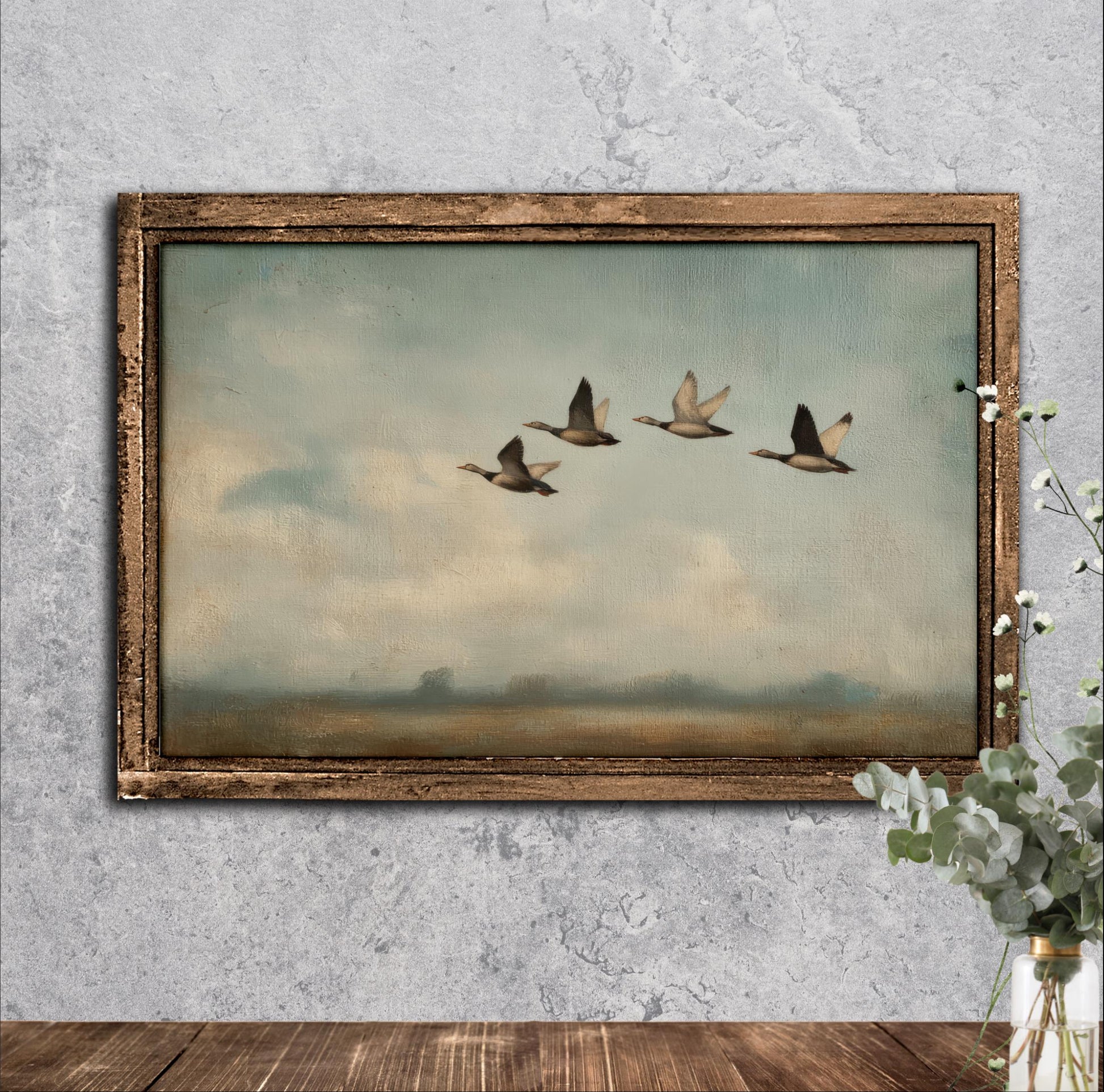 A framed painting of four ducks flying in a line against a cloudy sky is displayed on a wall.