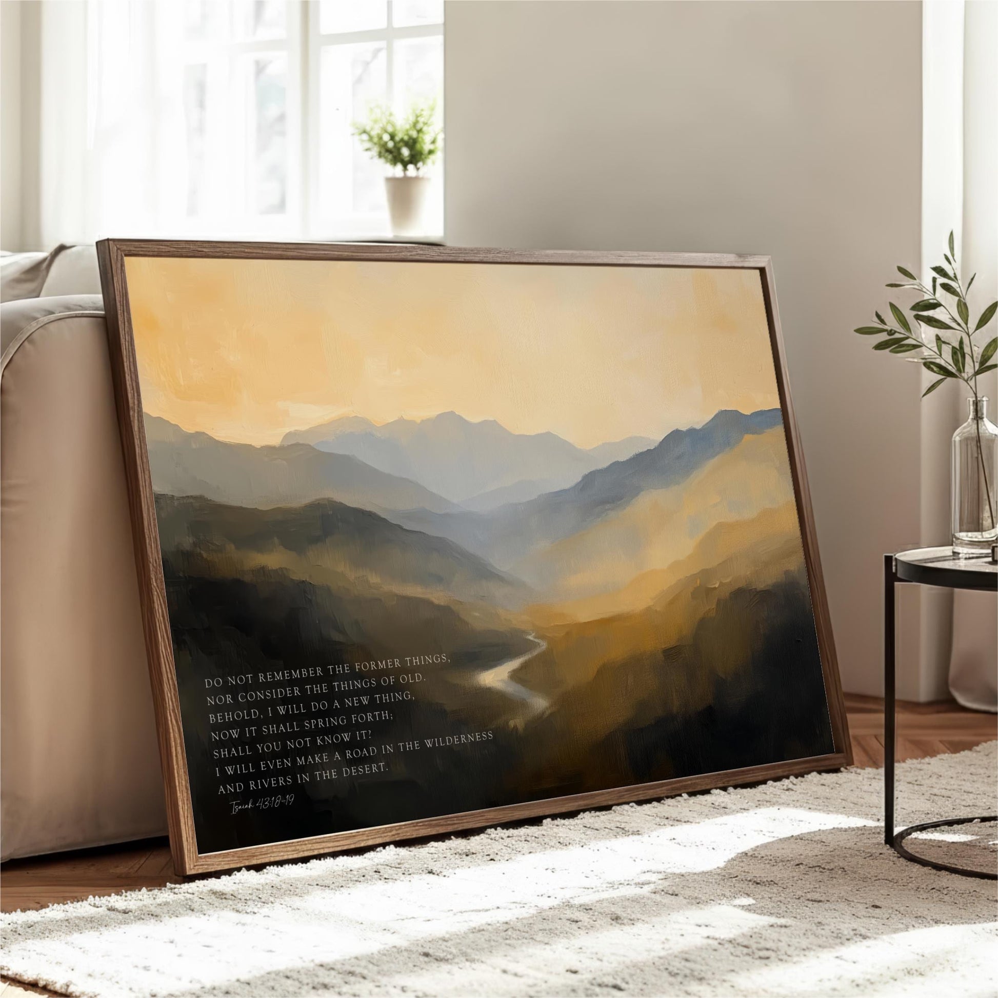 a large framed painting of a mountainous landscape with a river in the foreground, placed on a white rug in a living room setting.