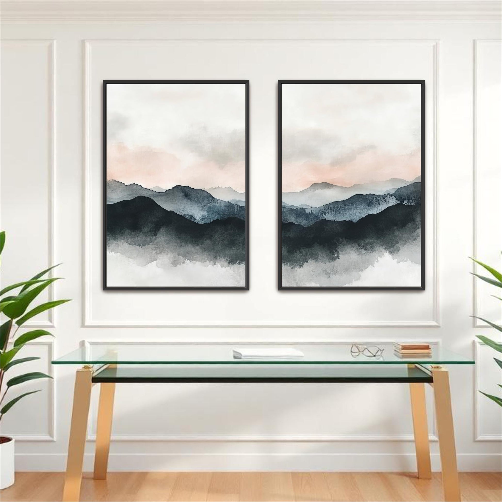 two framed watercolor paintings of mountains hanging on a white wall above a glass desk with a wooden frame.