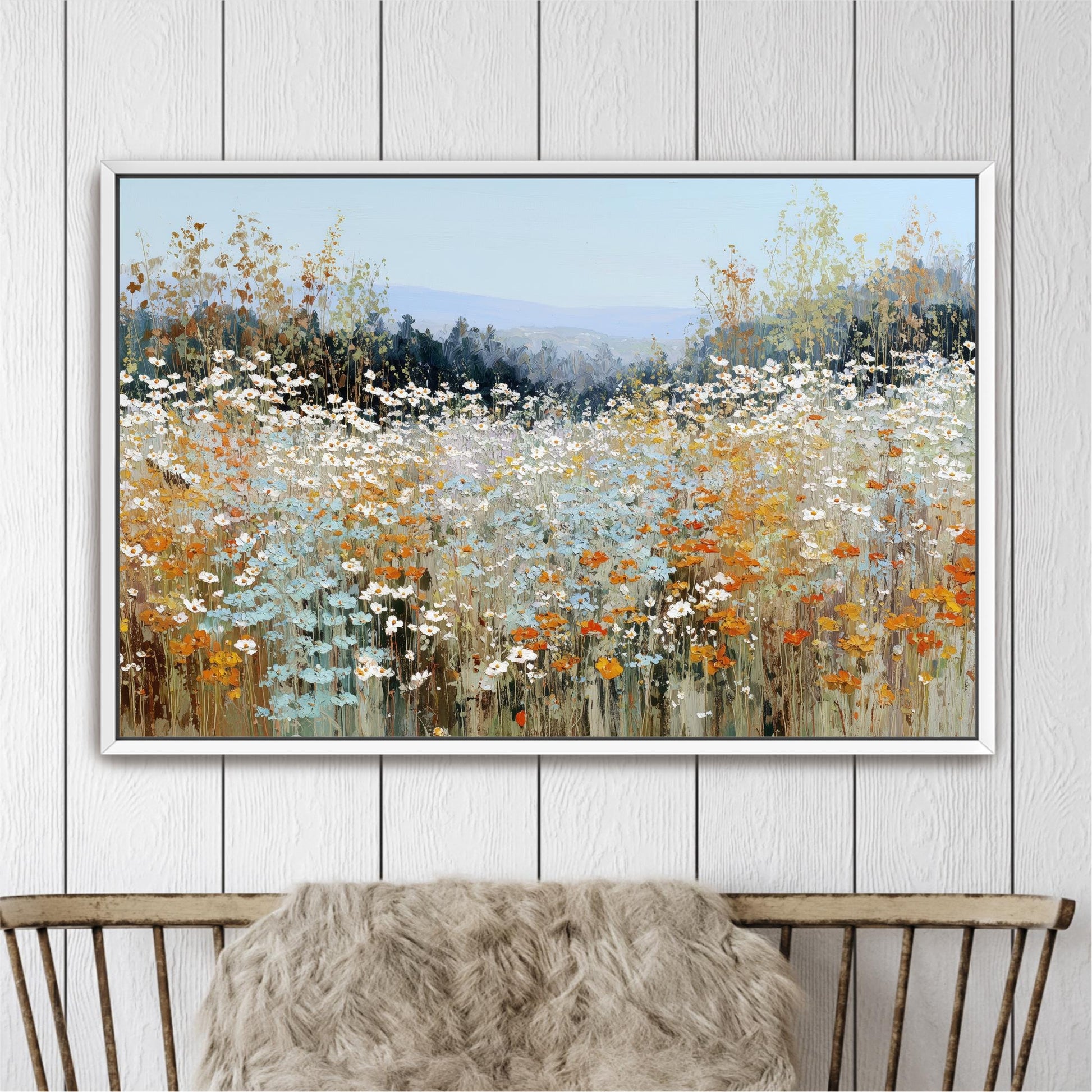 a large, framed painting of a field of flowers, with a mix of orange, white, and blue colors. The painting is displayed on a white wall above a wooden chair.
