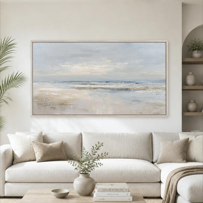 a large, framed painting of a serene beach scene hanging on a wall above a white sofa in a living room.
