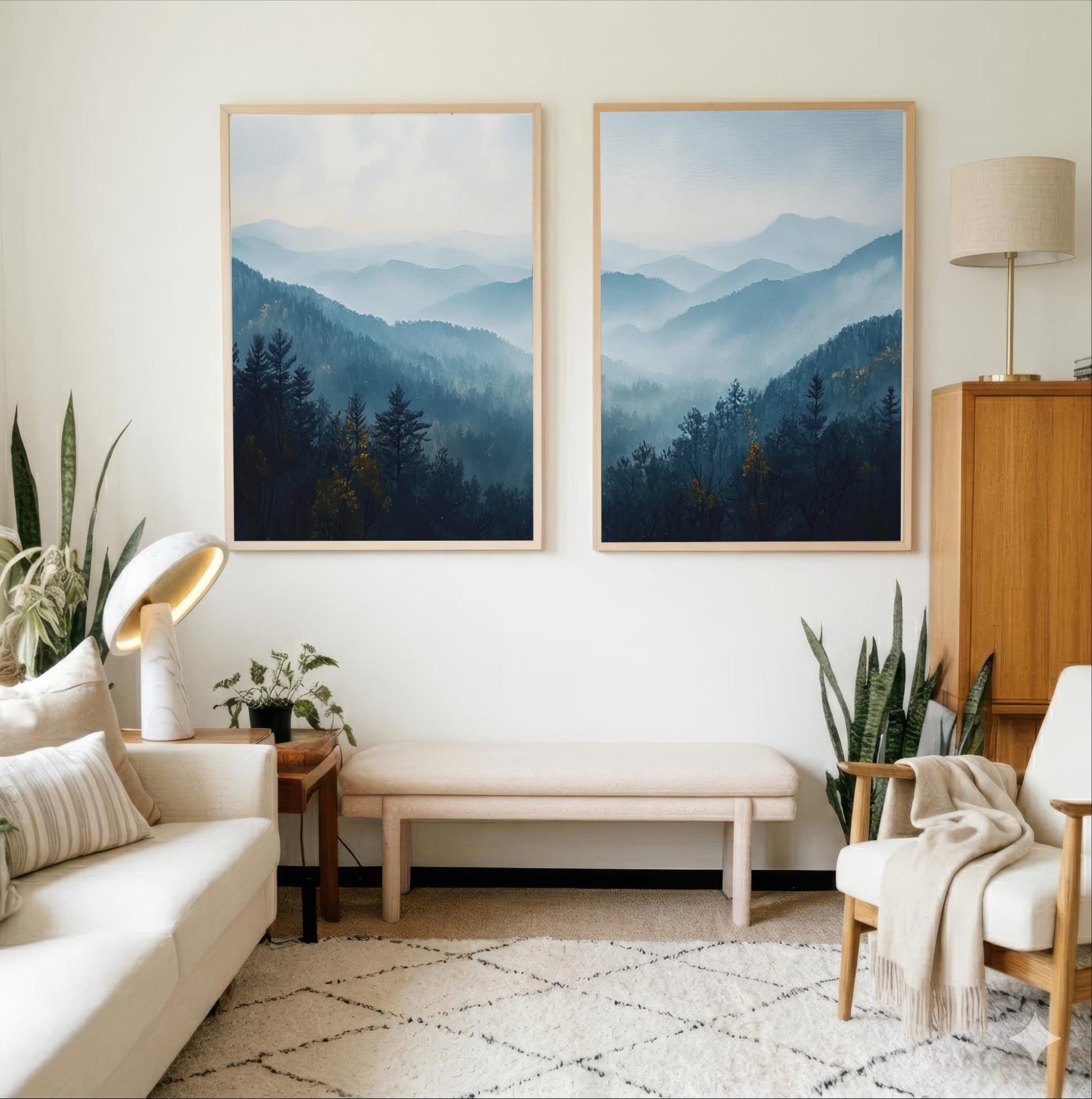 a serene living room with a white sofa, a wooden side table, and two framed landscape paintings of mountains and forests hanging on the wall.