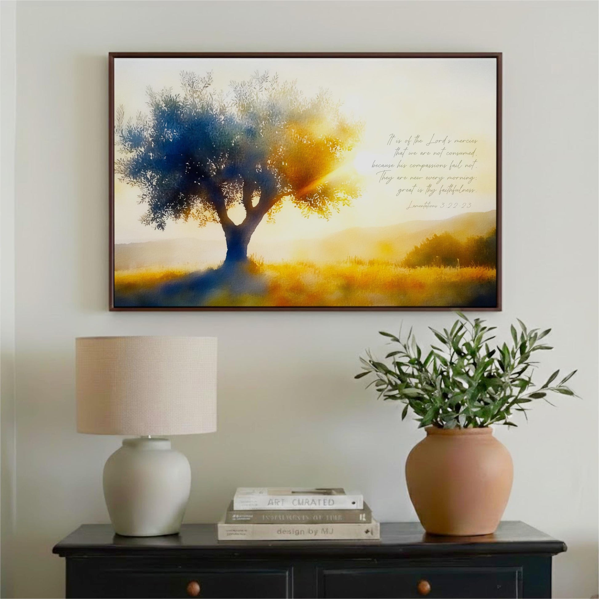a framed painting of a tree with a warm, golden glow, hanging on a wall above a wooden table with a lamp and a potted plant.