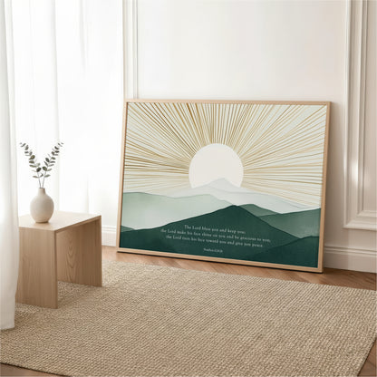 a large framed poster of a mountain landscape with a sunburst design, placed on a wooden floor in a room with a vase of greenery and a rug.