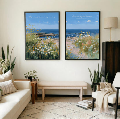 a living room with two framed paintings of a beach scene hanging on the wall. The paintings depict a serene landscape with a blue sky, ocean, and grassy area. The room is decorated with a white couch, a wooden side table, and a beige armchair. There are also several potted plants and books in the room, adding to the cozy and inviting atmosphere.
