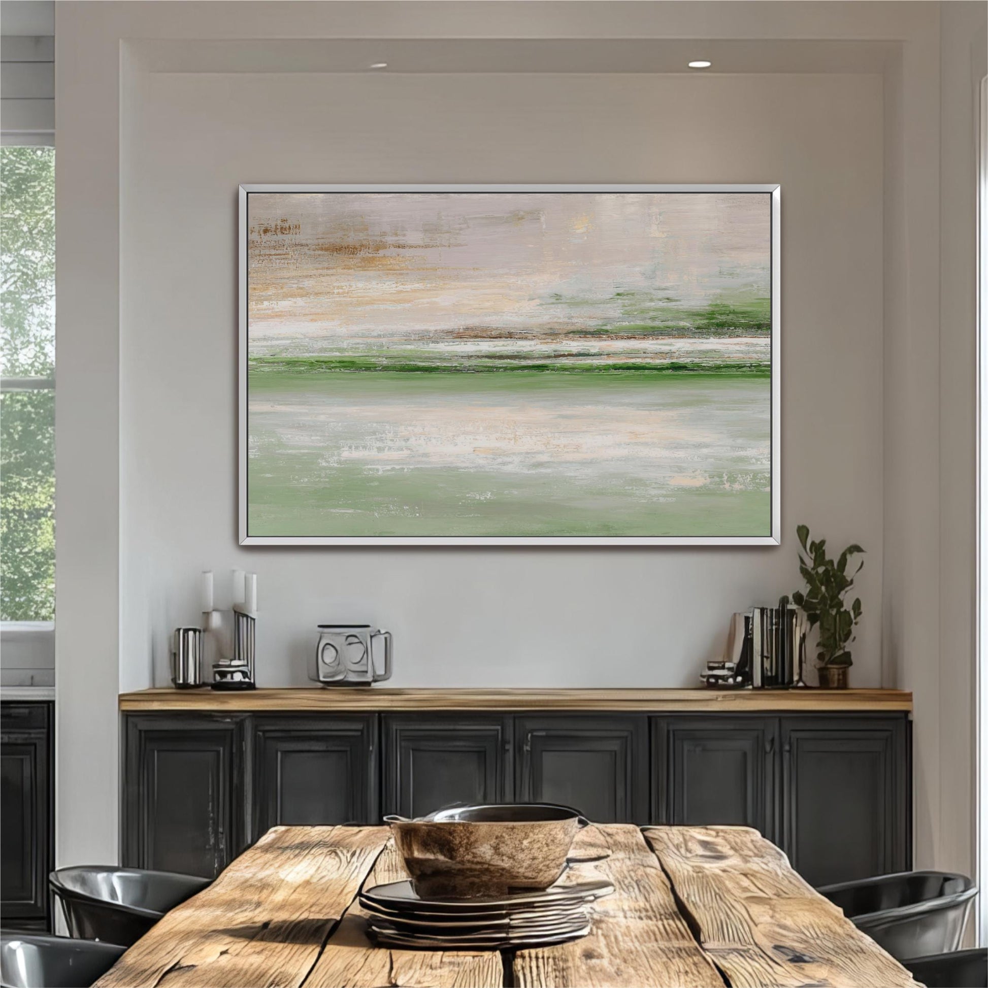 a large, abstract painting hanging on a white wall above a wooden dining table with black cabinets below it. The table is set with plates and bowls, and there are potted plants and other decorative items on the table.