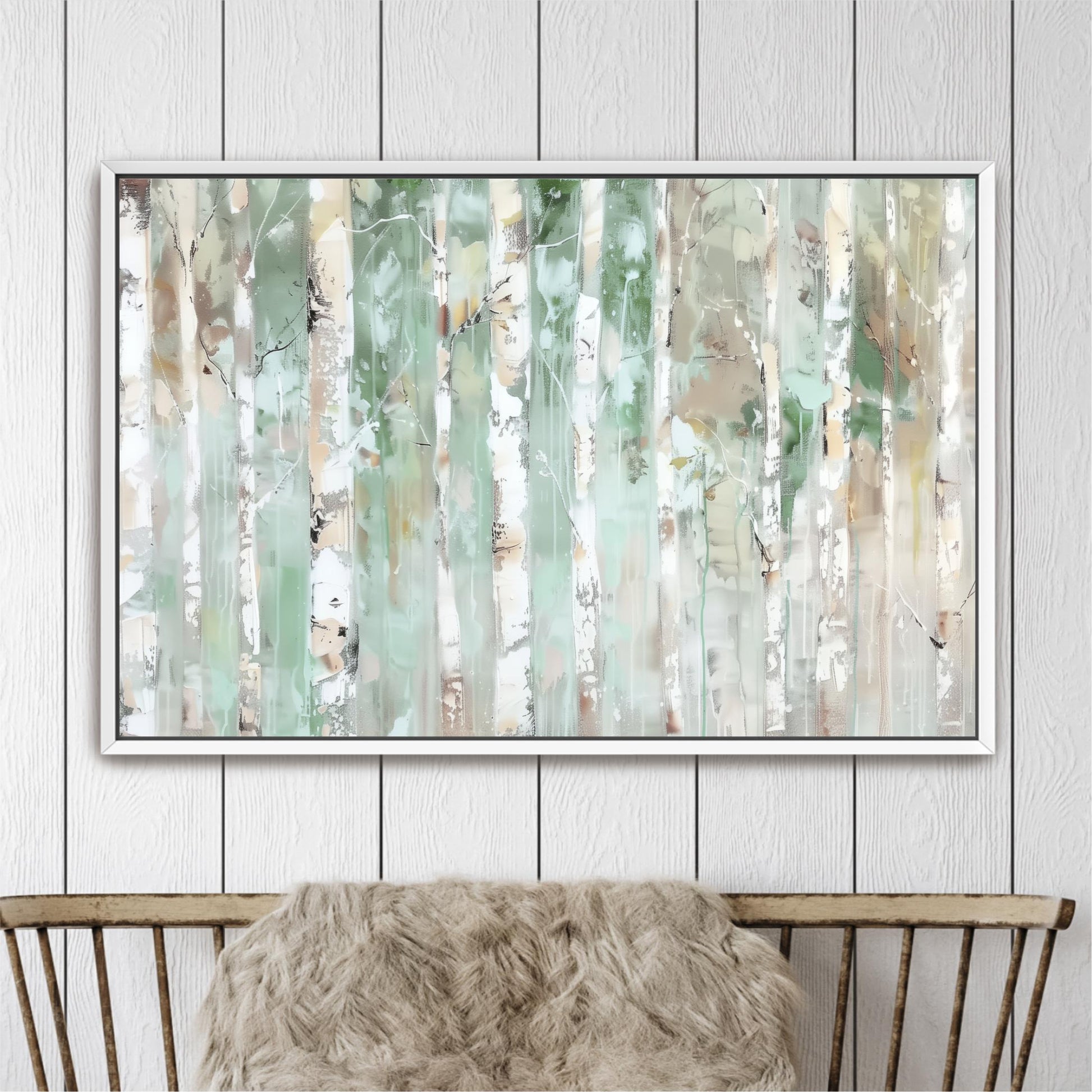 a large, framed painting of a forest scene with tall trees and a mix of green and white colors. The painting is hanging on a white wall above a wooden chair.