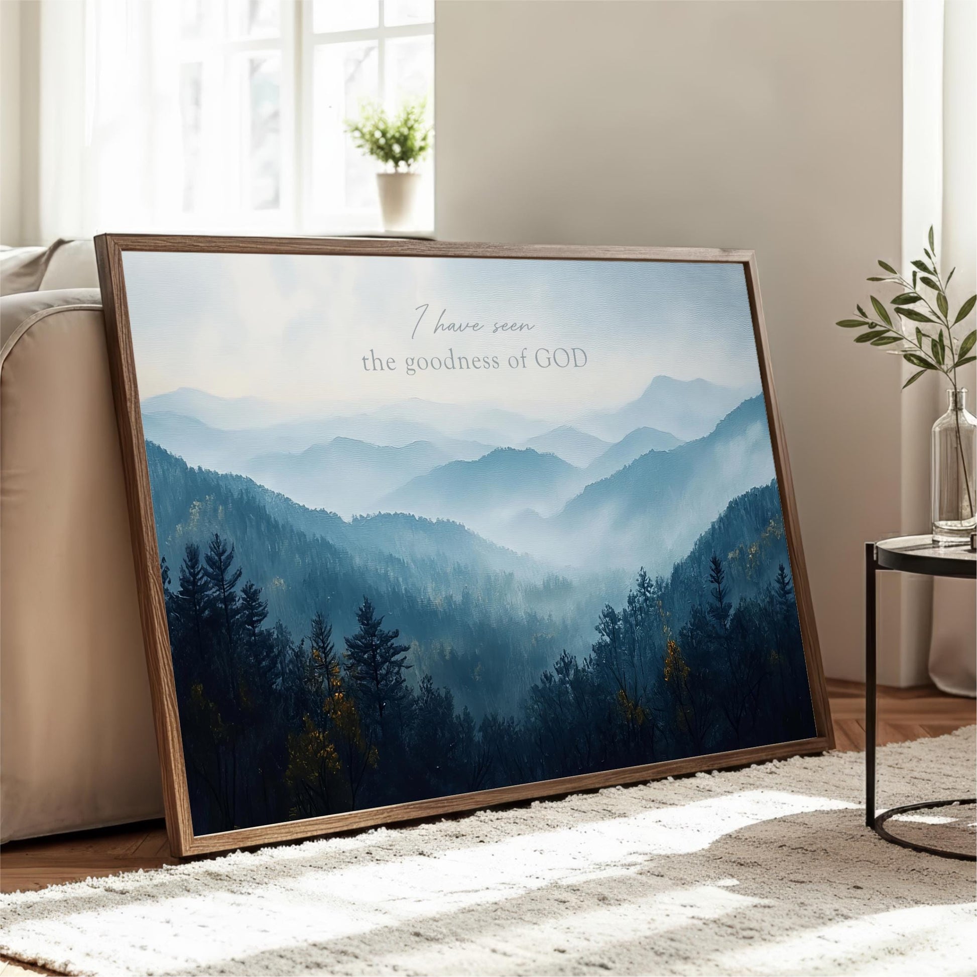 A framed landscape photograph depicting a mountainous, forested scene is displayed on a wooden stand in a living room.