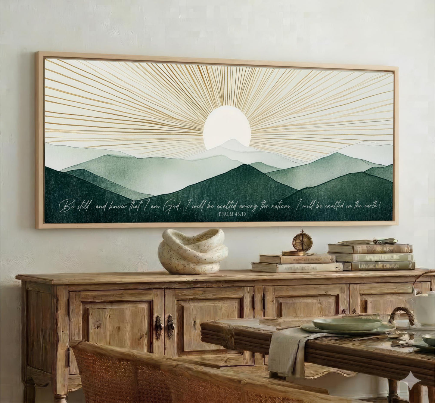 a large framed painting of a mountain landscape with a sun in the background, hanging on a wall above a wooden cabinet.