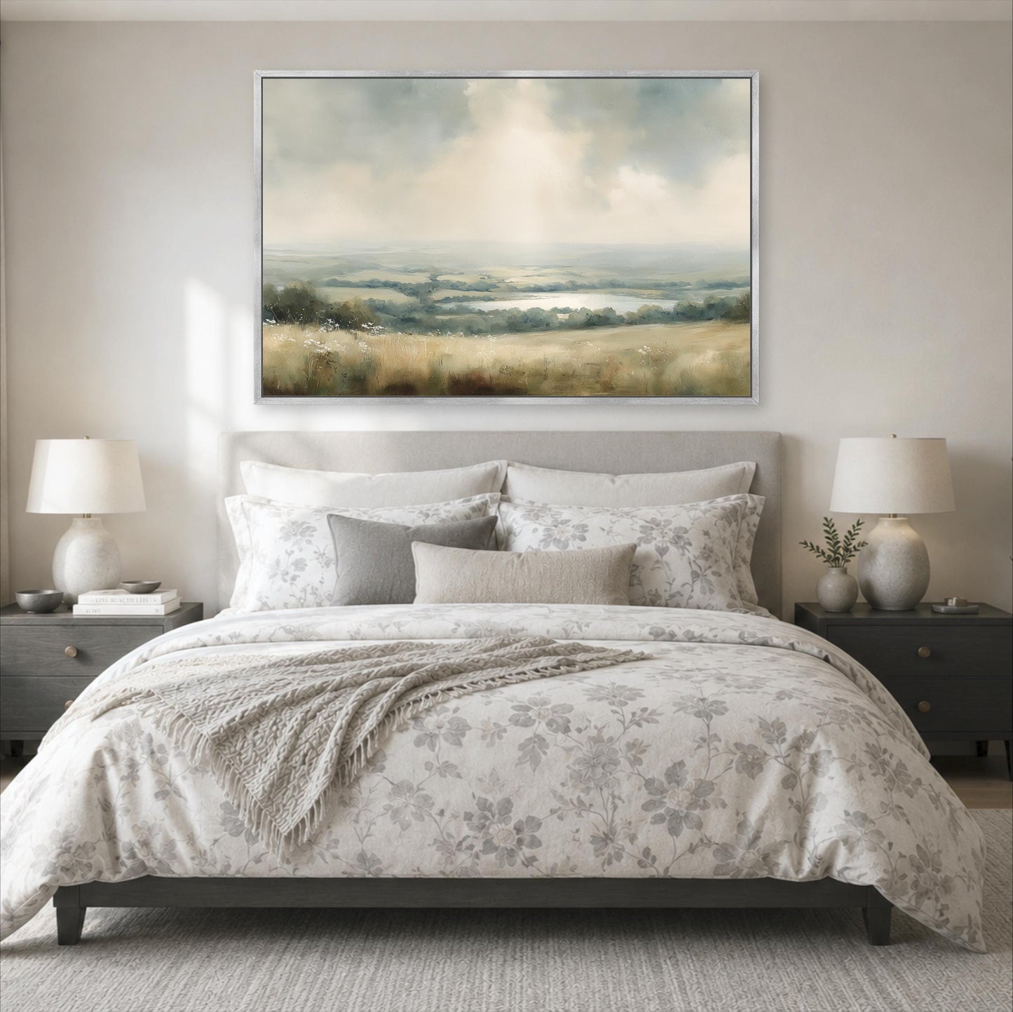 a serene bedroom scene with a large bed adorned with a floral comforter and pillows, flanked by two nightstands with lamps. Above the bed, a large landscape painting hangs on the wall, adding an artistic touch to the room's decor.