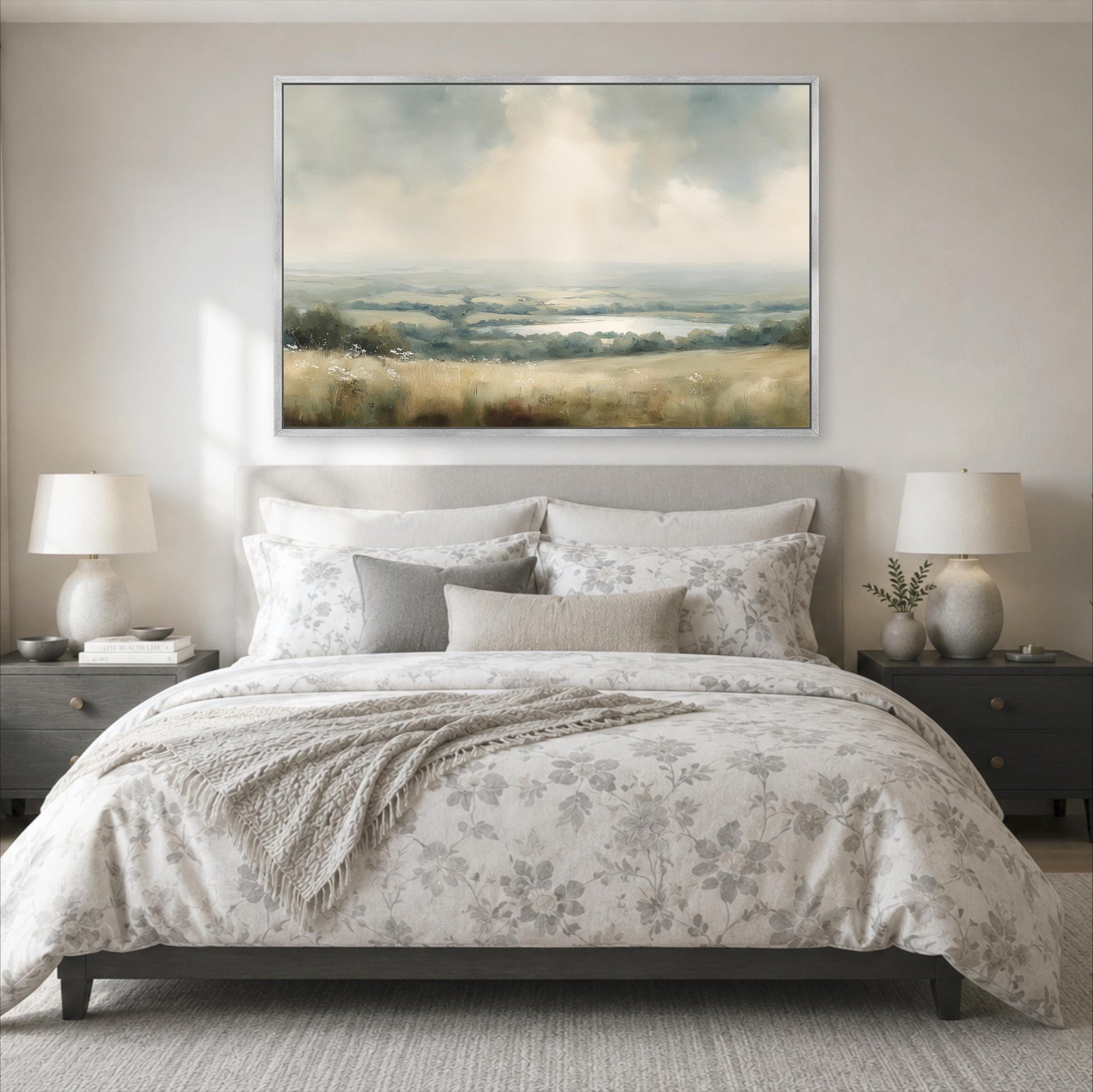 a serene bedroom scene with a large bed adorned with a floral comforter and pillows, flanked by two nightstands with lamps. Above the bed, a large landscape painting hangs on the wall, adding an artistic touch to the room's decor.