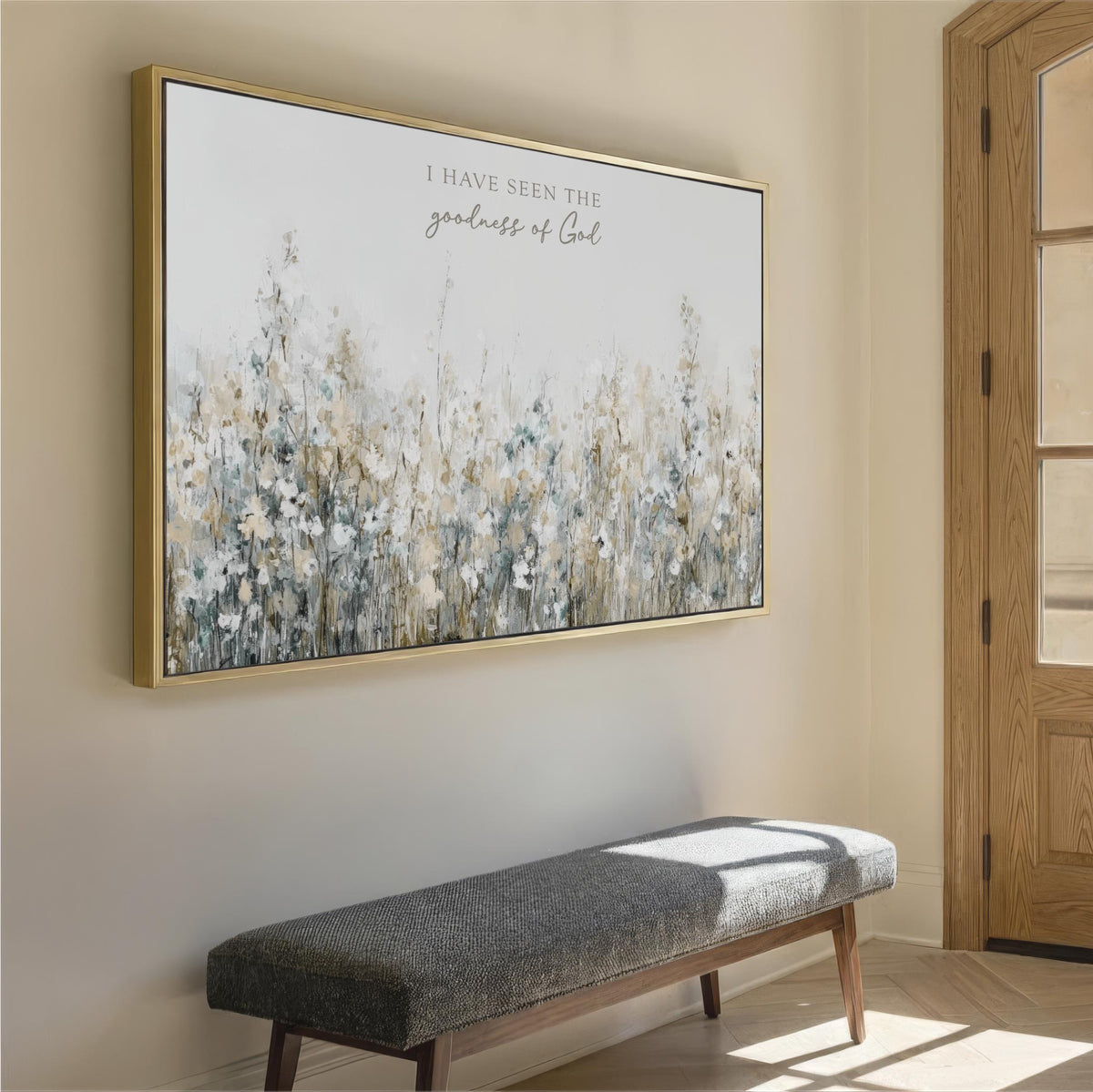 a large framed painting of a field of flowers hanging on a wall, with a gray bench placed in front of it.