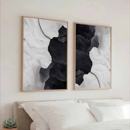 two large black and white abstract paintings hanging on a wall above a bed with white pillows.