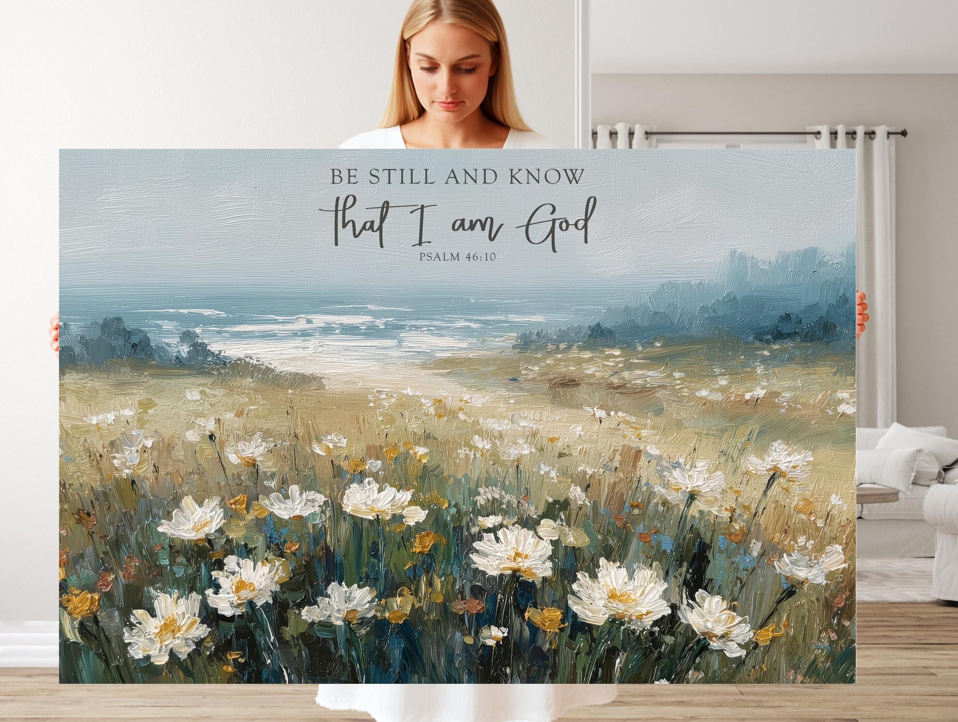 A woman is holding a large canvas print of a field of white flowers, with a blue sky and water in the background.