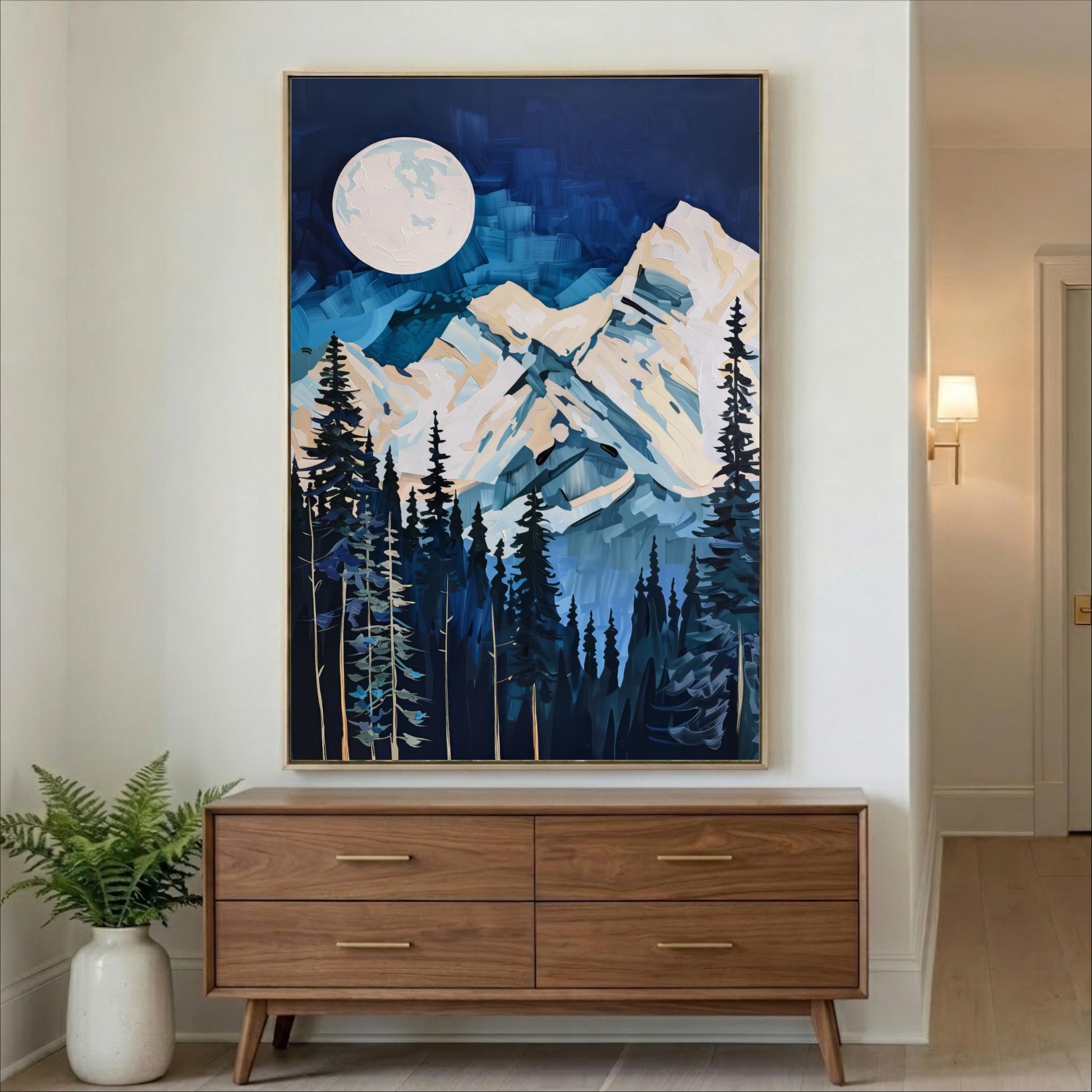 a large painting of a mountain landscape with a full moon in the night sky, hanging on a wall above a wooden dresser.