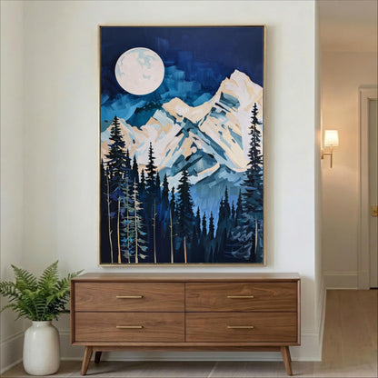 a large painting of a mountain landscape with a full moon in the night sky, hanging on a wall above a wooden dresser.