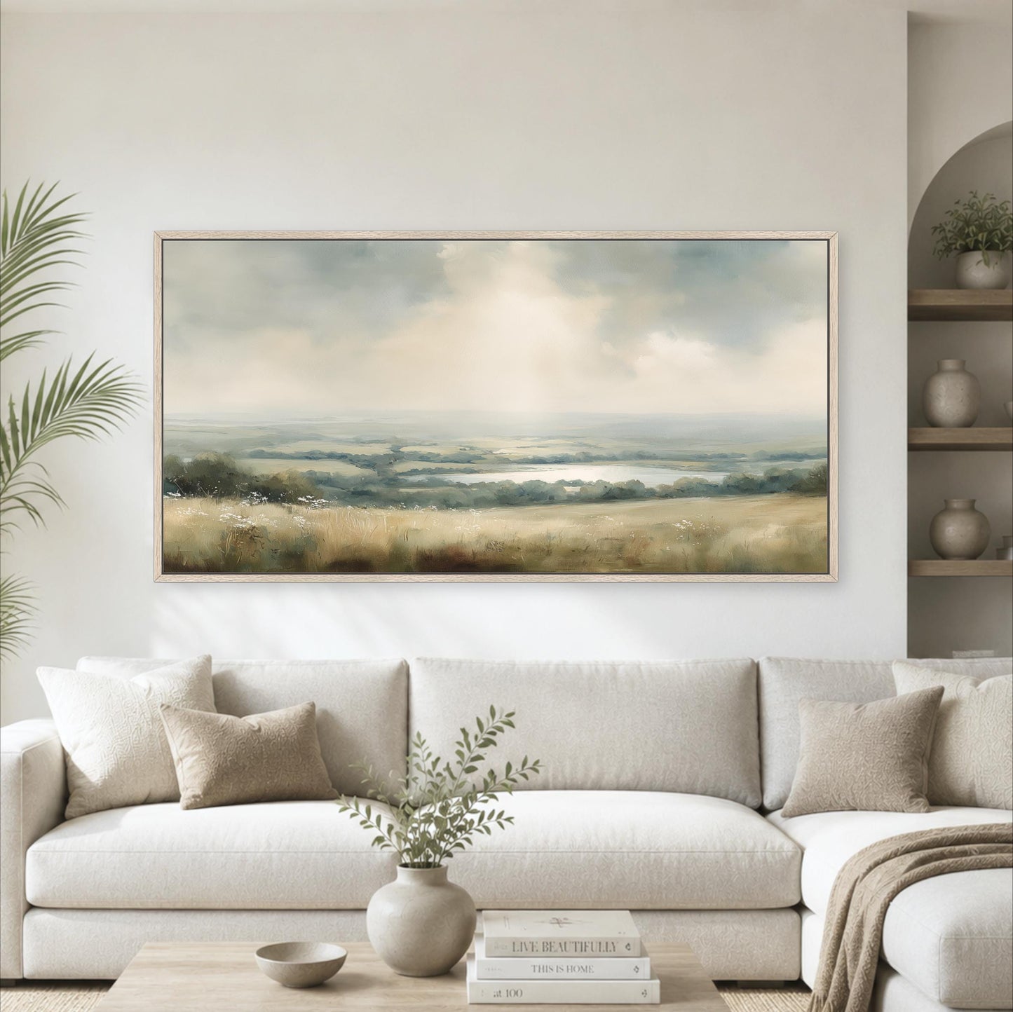 a large landscape painting hanging on a wall above a white sofa in a living room setting.