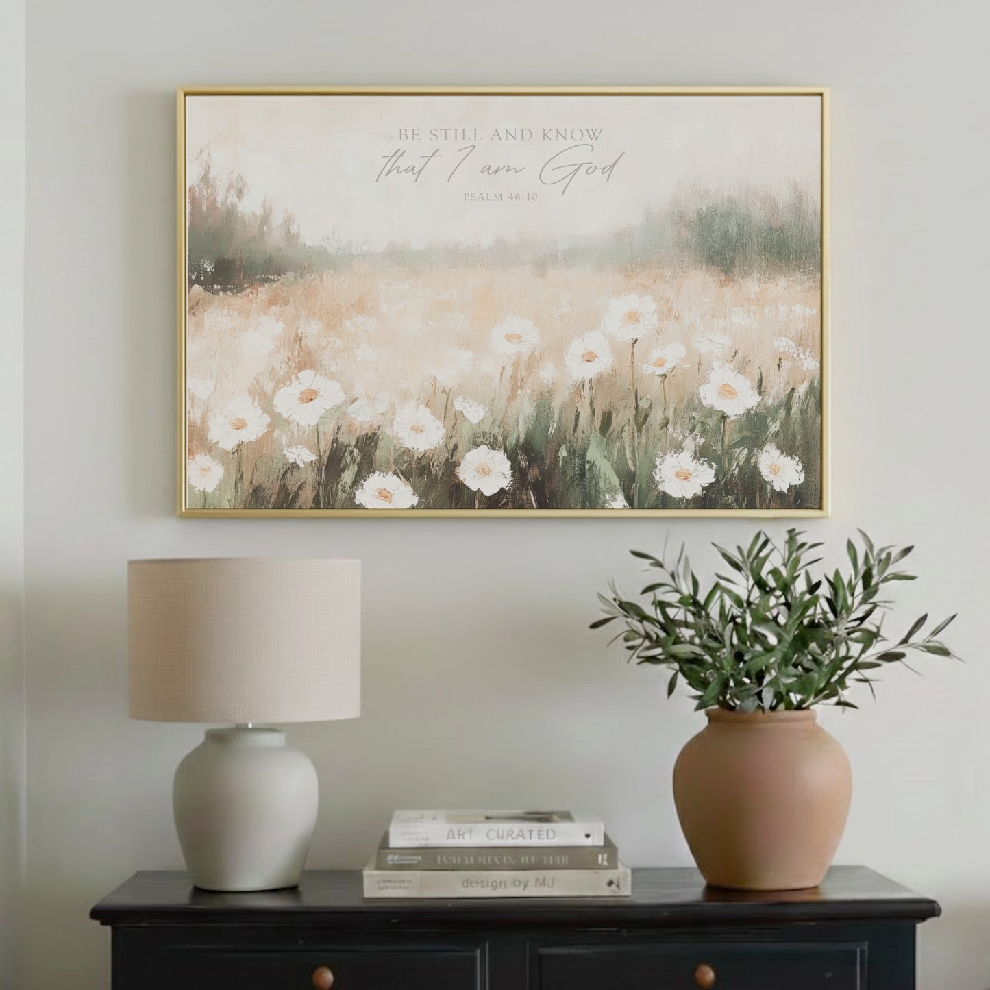 a framed painting of a field of white flowers hanging on a wall above a black dresser with a lamp and a potted plant.