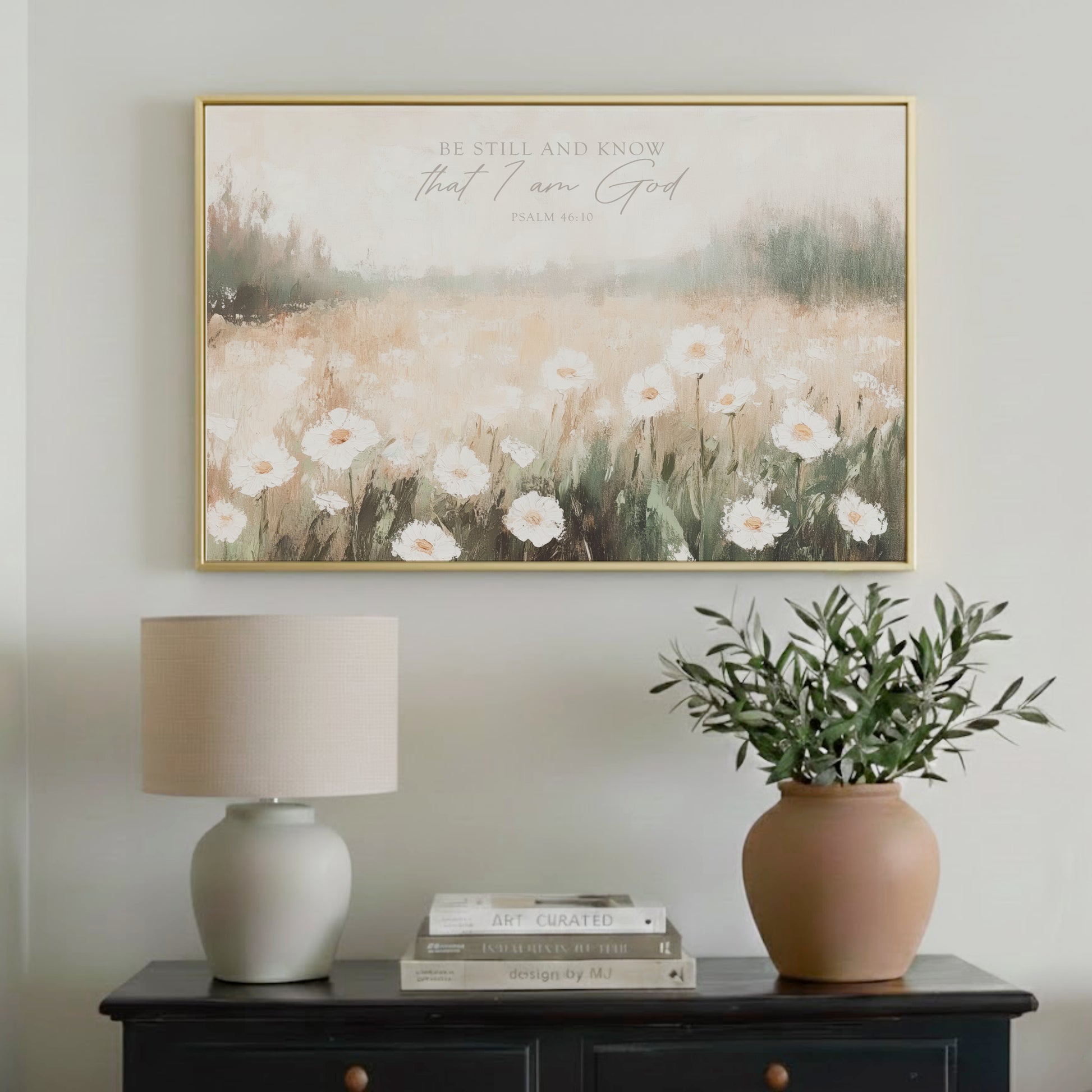a framed painting of a field of white flowers hanging on a wall above a black dresser with a lamp and a potted plant.