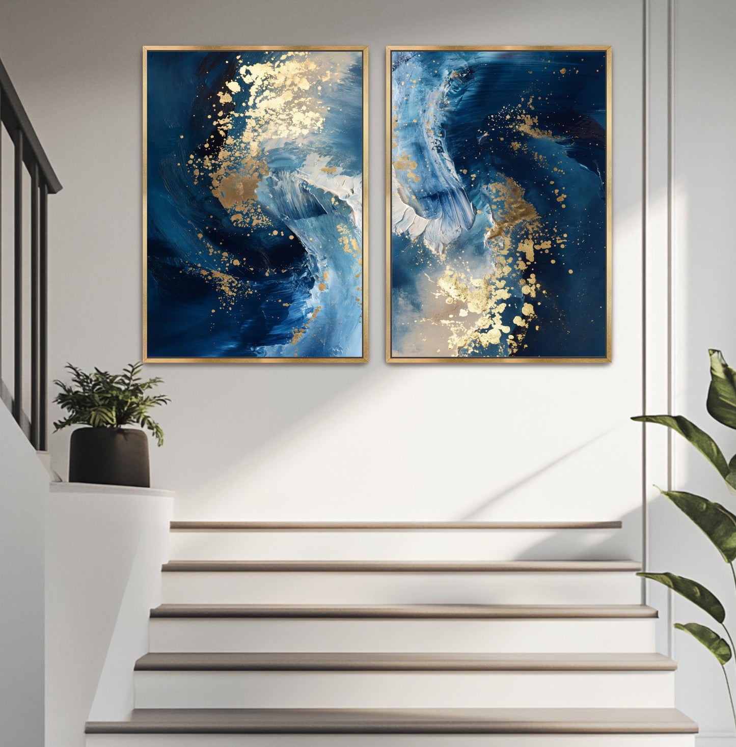 two large paintings hanging on a white wall above a set of stairs. The paintings are abstract and have a blue and white color scheme, with gold accents. A potted plant is located on the left side of the stairs, and a plant is visible on the right side of the stairs.