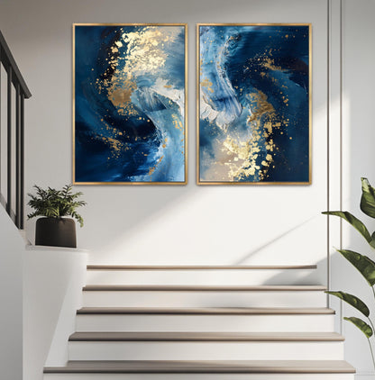 two large paintings hanging on a white wall above a set of stairs. The paintings are abstract and have a blue and white color scheme, with gold accents. A potted plant is located on the left side of the stairs, and a plant is visible on the right side of the stairs.