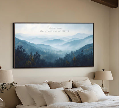 a large framed picture of a mountain landscape with trees and mountains in the background, hanging on a wall above a bed with white bedding.