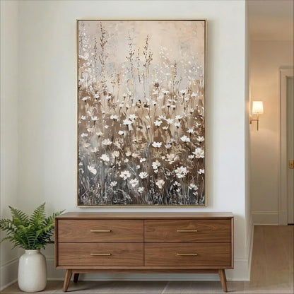 a large painting of white flowers hanging on a wall above a wooden dresser with four drawers.