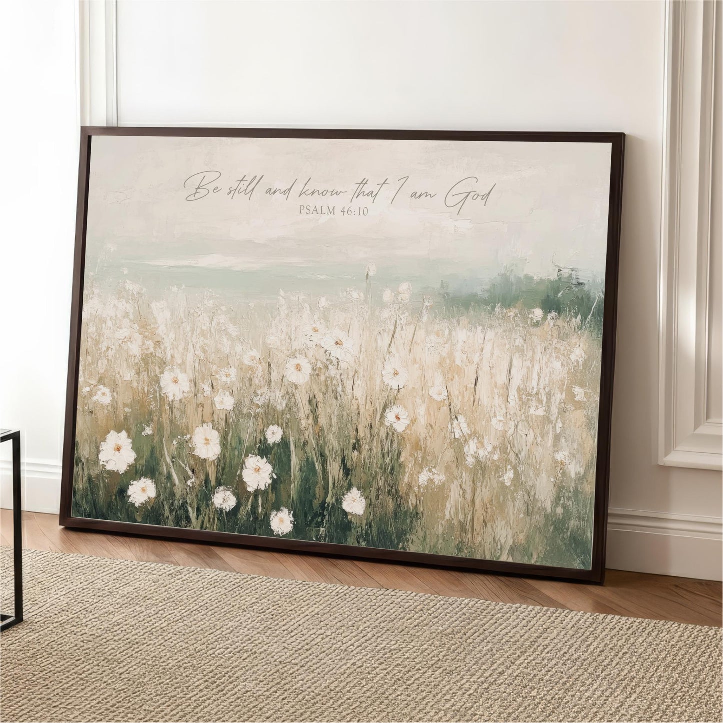 A framed painting depicting a field of white flowers against a pale green background, with a text overlay that reads "Be still and know that I am God" from Psalm 46:1.