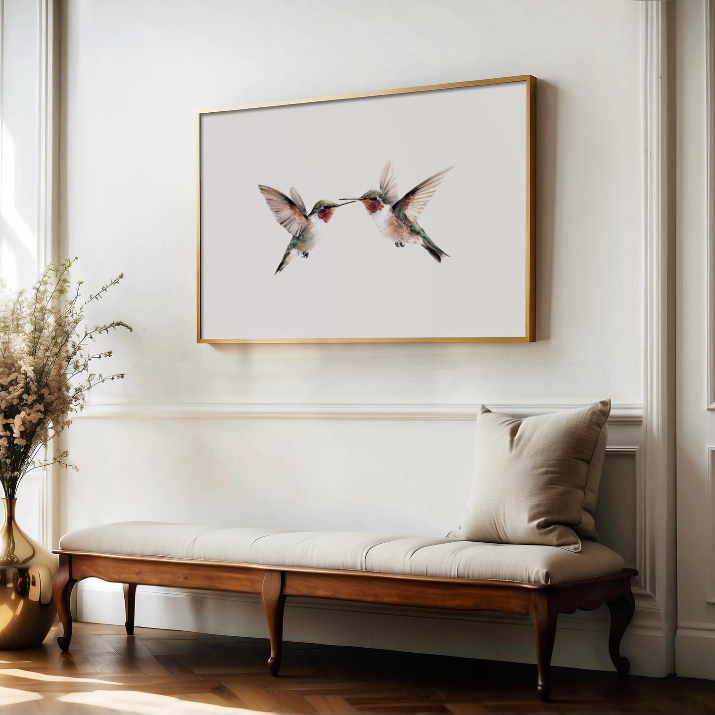 a wooden bench with a white cushion, positioned in front of a framed picture of two hummingbirds. The bench is situated in a room with white walls and a wooden floor.